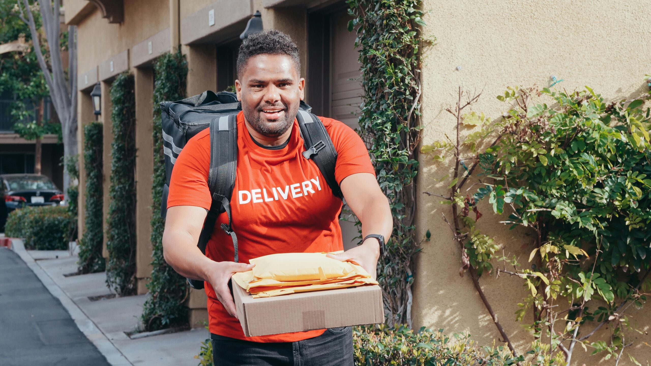 Friendly deliveryman in red delivering packages outdoors on a sunny day.
