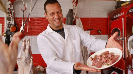 Happy butcher in white coat presenting a plate of fresh meat in a colorful butcher shop.